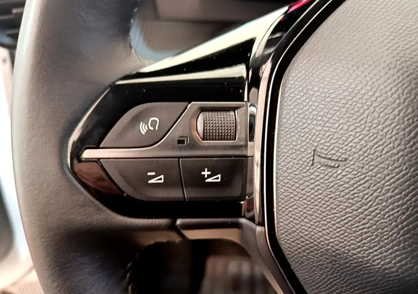 Gros plan sur les commandes gauche du volant cuir noir du Peugeot 208 blanc, avec boutons multifonctions.