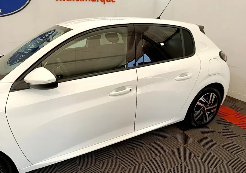 Vue de profil côté gauche d'une Peugeot 208 blanche PureTech 100 S&S Allure Business avec jantes alliage et vitres teintées.