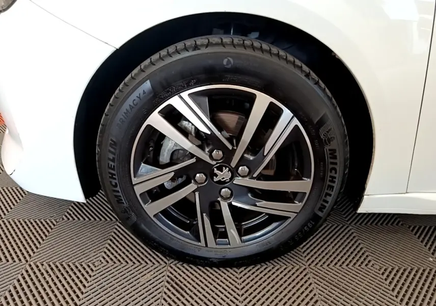 Gros plan sur la roue avant droite d'une Peugeot 208 blanche, jante alliage noire et argent avec pneu Michelin.