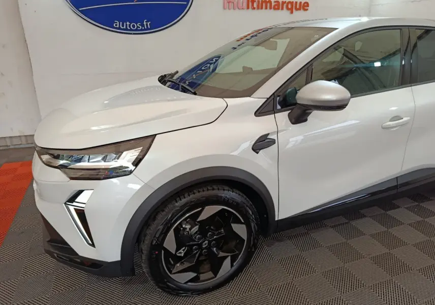 Vue 3/4 avant droit du Renault Captur blanc avec jantes noires et détails de phares LED modernes.