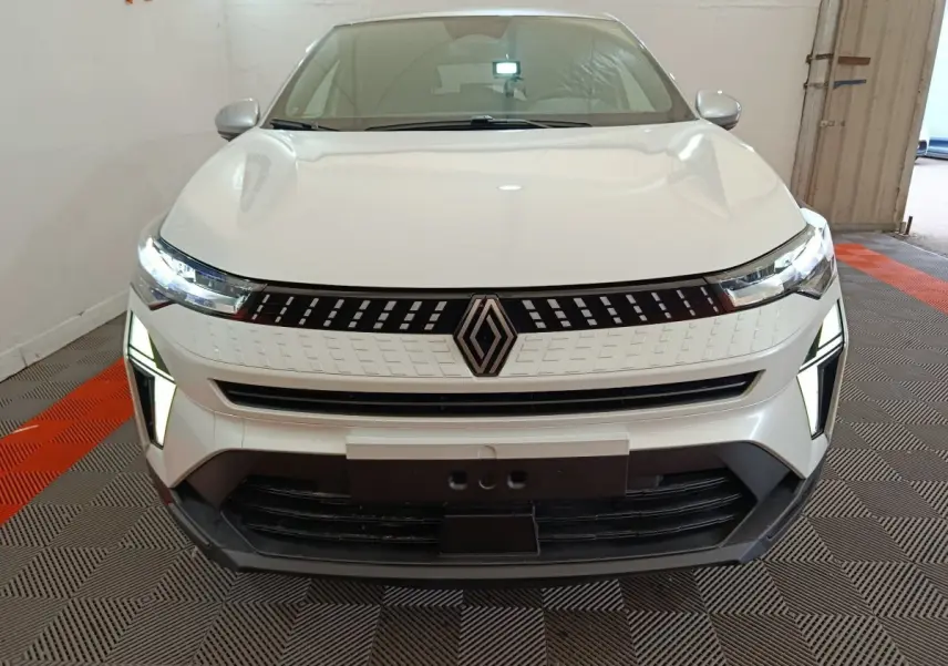 Vue de face du Renault Captur blanc 2025 avec phares LED allumés et calandre moderne en intérieur showroom.