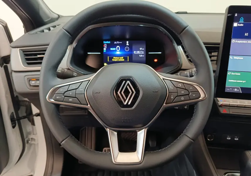 Vue rapprochée du volant en cuir noir du Renault Captur blanc 2025 avec tableau de bord numérique et écran tactile central.
