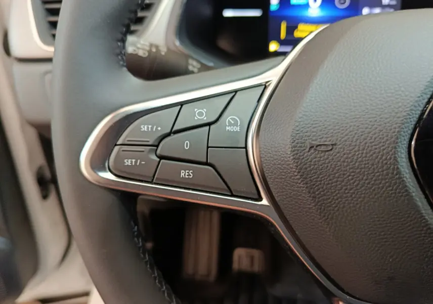 Gros plan sur les commandes au volant côté gauche du Renault Captur blanc techno E-Tech 2025 avec affichage numérique en arrière-plan.