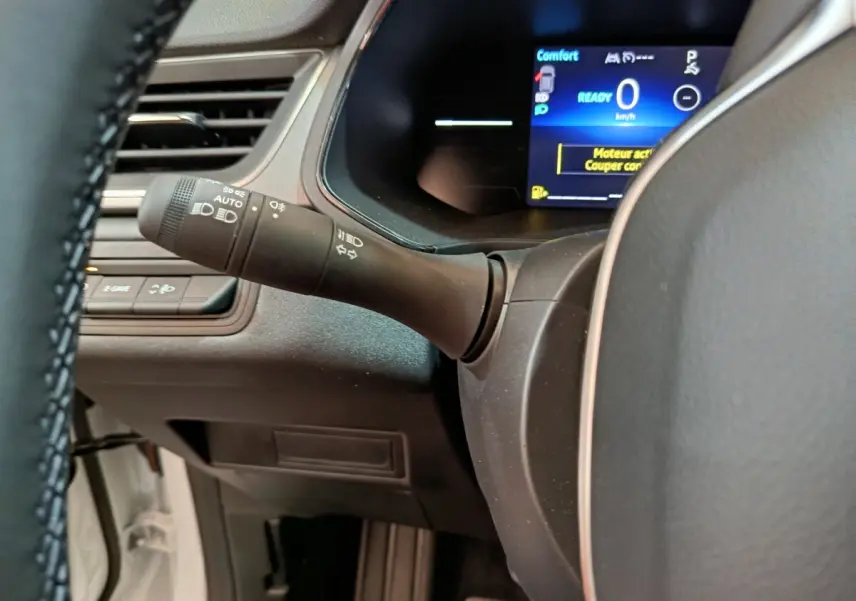 Gros plan sur la manette d'éclairage à gauche du volant cuir synthétique du Renault Captur blanc, tableau de bord numérique visible.