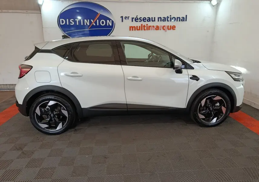 Profil côté gauche du Renault Captur blanc 2025 avec jantes noires et toit noir contrastant en intérieur showroom.