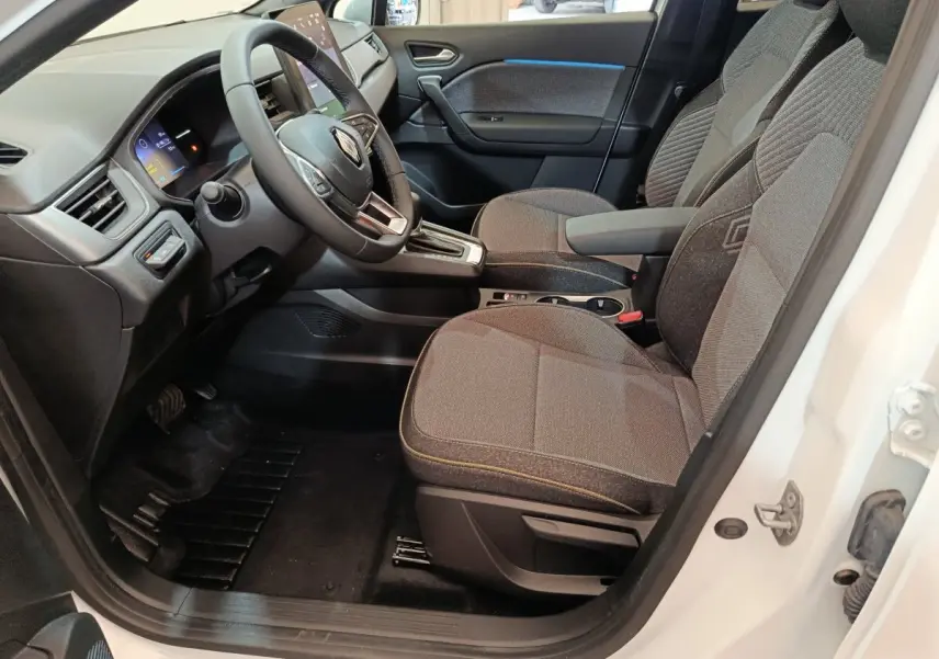 Intérieur avant droit du Renault Captur blanc 2025, sièges gris, volant multifonctions et écran tactile visible.
