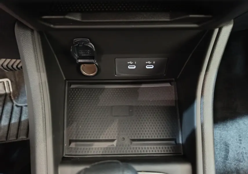 Gros plan sur la console centrale du Renault Captur blanc 2025, montrant prises USB et prise 12V dans un espace de rangement noir.