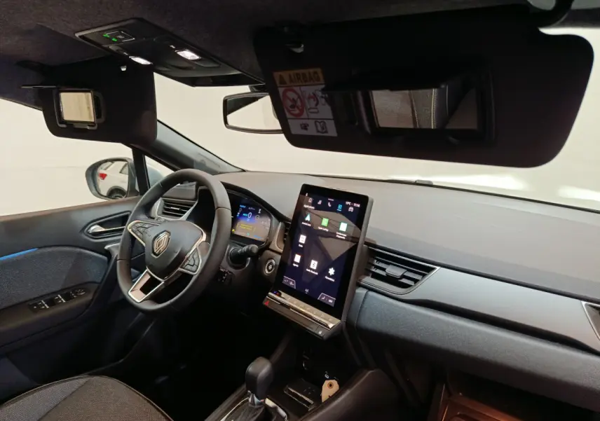 Vue intérieure côté conducteur du tableau de bord du Renault Captur blanc 2025 avec écran tactile vertical et volant multifonctions.