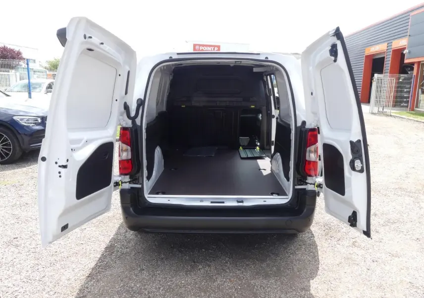 Vue arrière du Peugeot Partner blanc 2025 avec portes ouvertes montrant l'espace de chargement vide et plancher bois antidérapant.