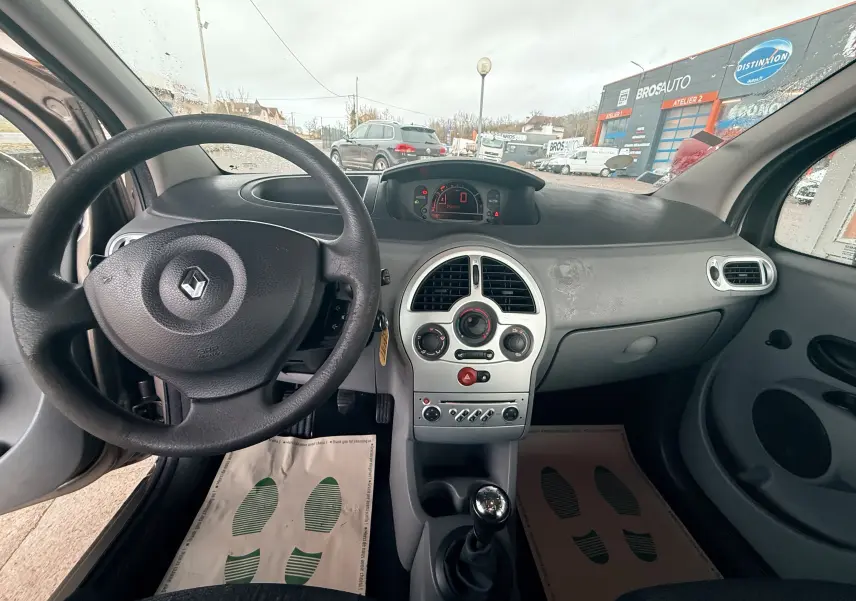 Vue intérieure avant de la Renault Modus beige, montrant le volant, tableau de bord et levier de vitesse manuel.