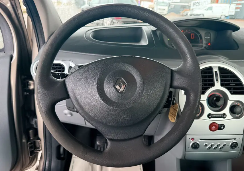 Vue centrée sur le volant noir avec logo Renault, tableau de bord et console centrale d’une Renault Modus beige 2011.