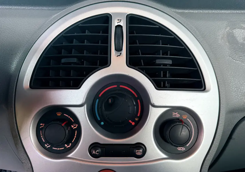 Gros plan sur la sortie d'air centrale ronde et la commande de chauffage du tableau de bord gris du Renault Modus beige.