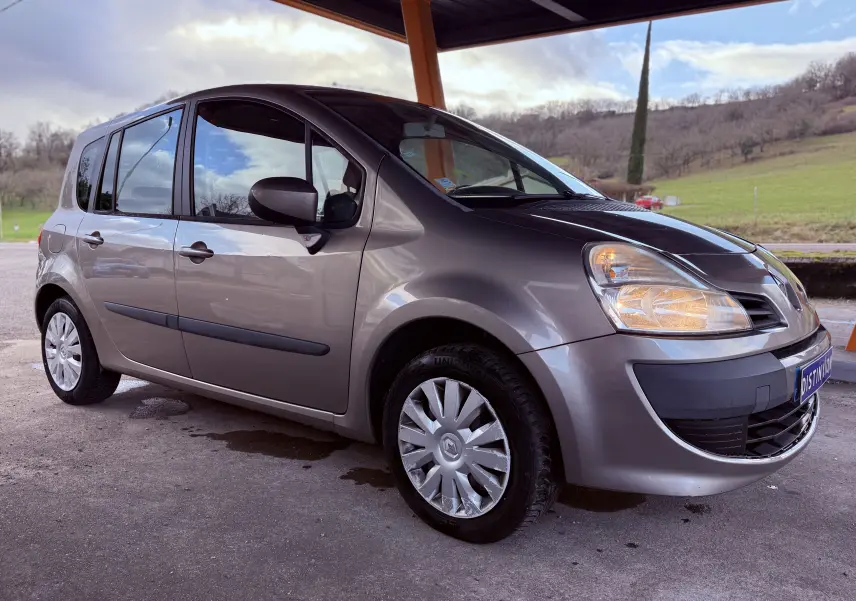 Renault Modus beige vue 3/4 avant droit sous abri, phare avant droit allumé et jantes avec enjoliveurs.