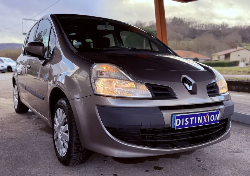 Renault Modus beige vue 3/4 avant droit avec phares allumés et plaque Distinxion visible.