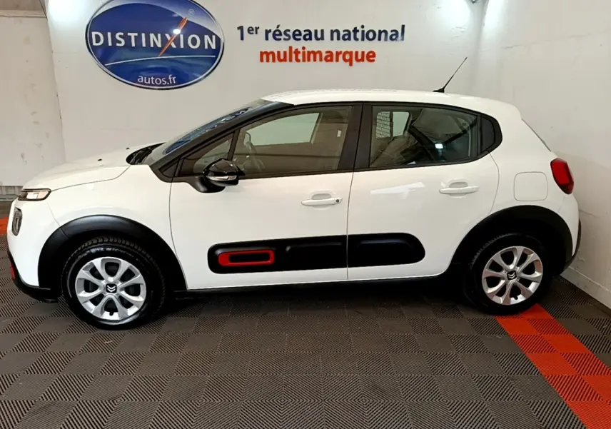 Vue de profil côté gauche d'une Citroën C3 blanche avec inserts noirs et rouge sur les portes, en intérieur showroom.