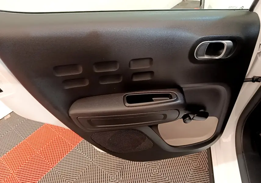 Vue rapprochée de la porte avant gauche noire et beige d'une Citroën C3 blanche, avec poignée et commande manuelle de vitre.
