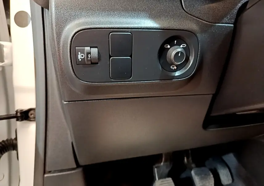 Détail intérieur côté gauche du tableau de bord noir de la Citroën C3 blanche, avec commandes des phares et rétroviseurs.