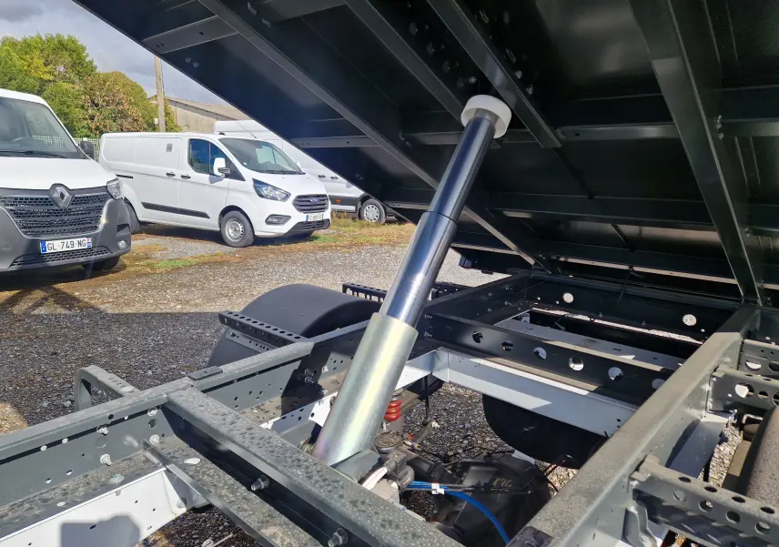 Vue rapprochée sous la benne relevée du Ford Transit Chassis Cabine blanc, mettant en valeur le vérin hydraulique et le châssis.