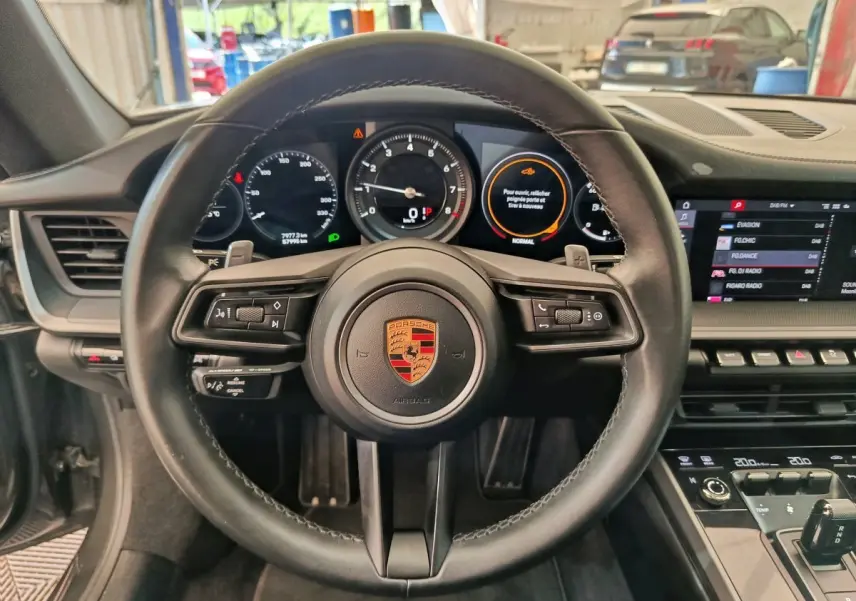 Vue intérieure centrée sur le volant cuir de la Porsche 911 Carrera 4S 2019 avec tableau de bord digital et écran tactile.