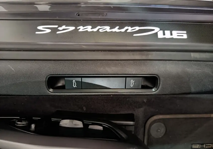 Gros plan sur la plaque de seuil de porte avec inscription Carrera 4S blanche sur fond gris foncé d'une Porsche 911.