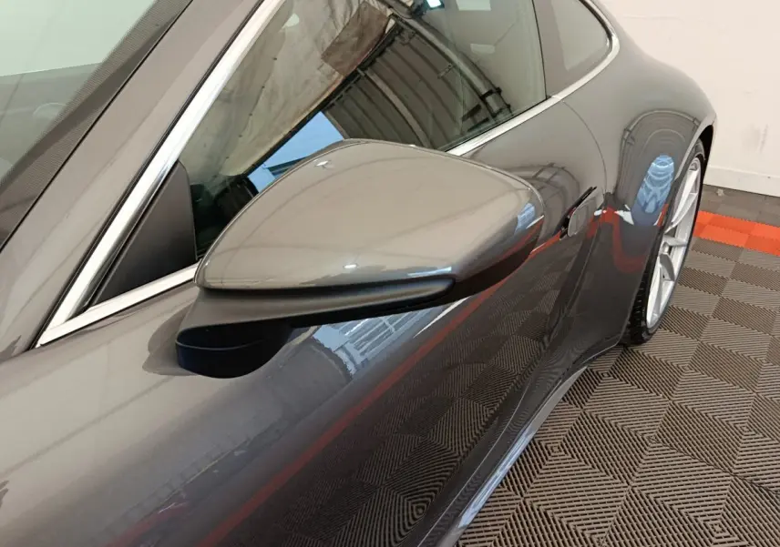 Gros plan sur le rétroviseur côté gauche d'une Porsche 911 Carrera 4S Coupé gris foncé, avec la porte et la roue arrière visibles.