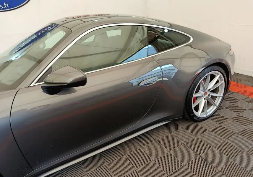 Profil côté gauche d'une Porsche 911 Carrera 4S Coupé gris foncé, mettant en valeur la jante alliage et la ligne fluide du toit.