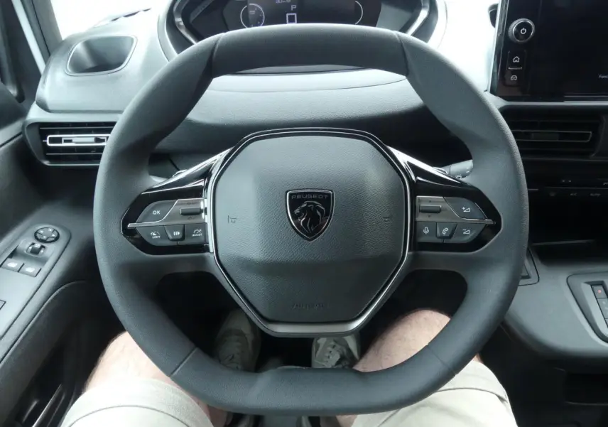 Vue rapprochée du volant multifonctions noir du Peugeot Partner 2025, avec tableau de bord et commandes visibles.