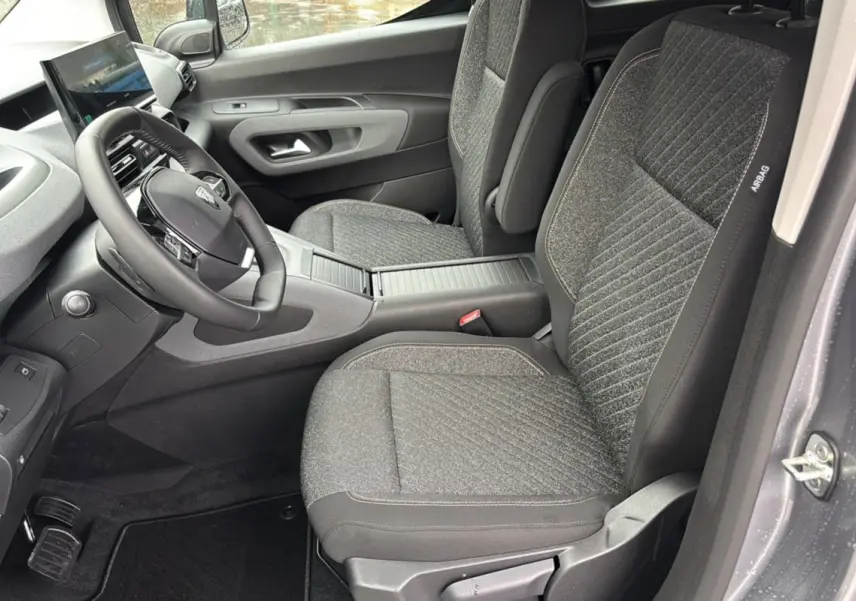 Vue intérieure côté conducteur du Peugeot Rifter gris artense, mettant en valeur les sièges tissu et le volant multifonctions cuir.