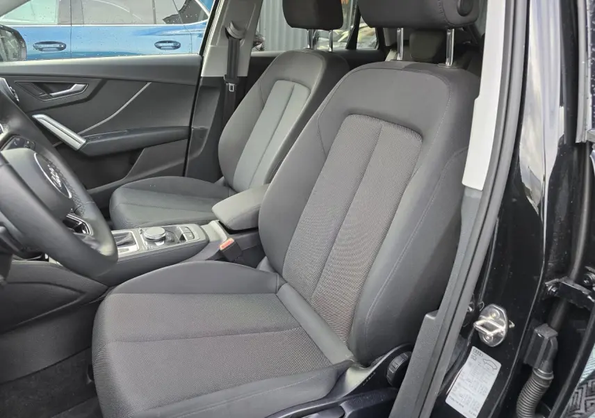 Vue intérieure côté conducteur de l'Audi Q2 35 TFSI 2023 noir mythic, sièges tissu gris et console centrale visible.