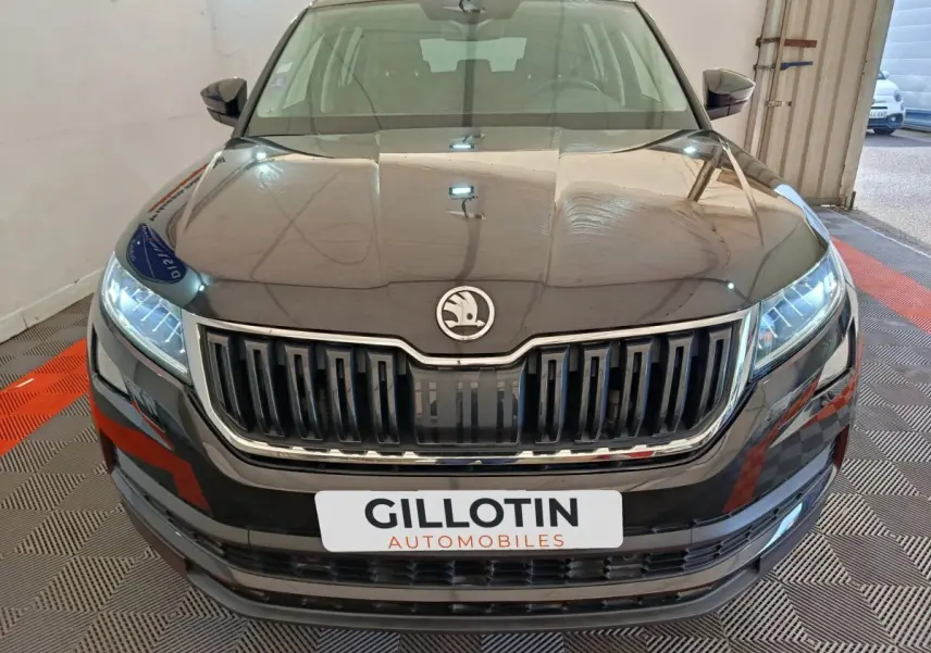 Vue frontale rapprochée d'un Skoda Kodiaq noir avec calandre verticale chromée et phares LED allumés.