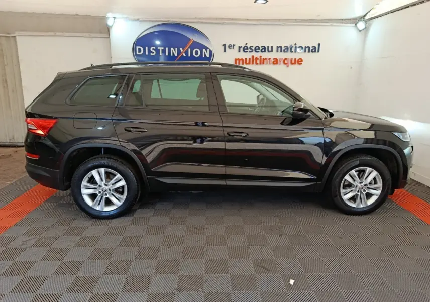 Profil côté droit d'un SUV SKODA KODIAQ noir 2021 garé en intérieur avec jantes alliage et barres de toit noires.