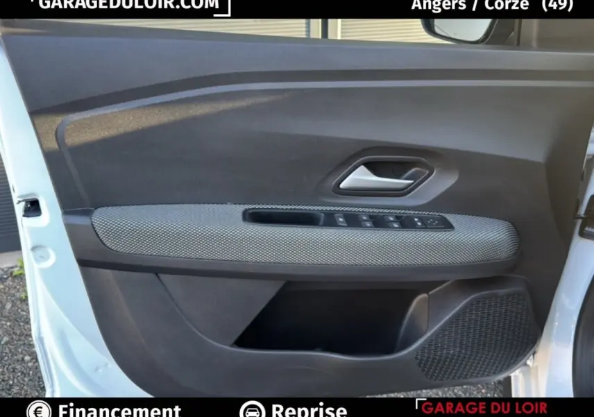 Intérieur de la porte avant gauche d'une Dacia Sandero blanche 2025, avec habillage tissu gris et commandes électriques.