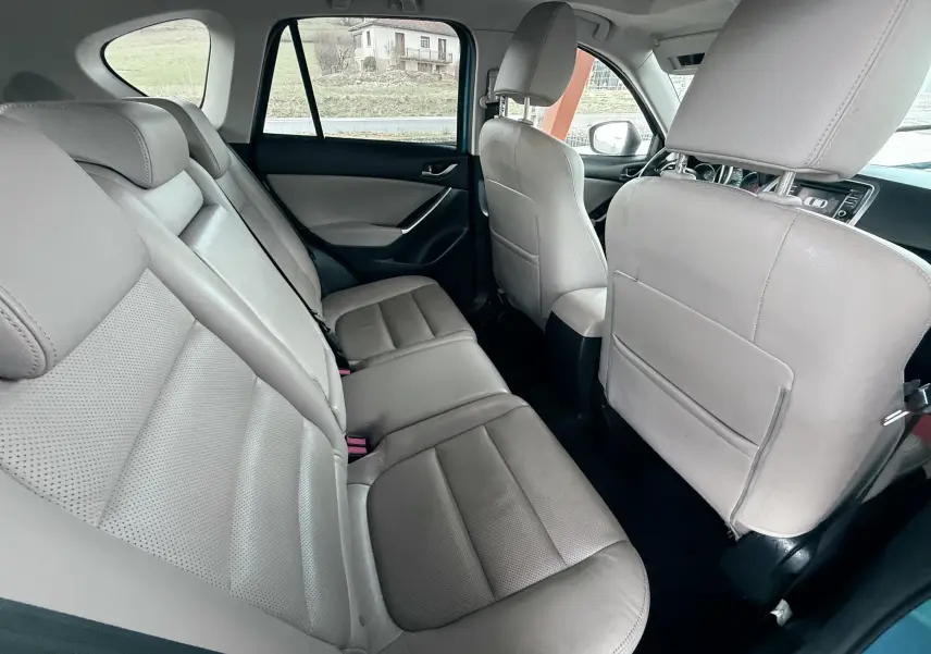 Vue intérieure arrière montrant les sièges en cuir beige du Mazda CX-5 2013, avec détails des portes et fenêtres.