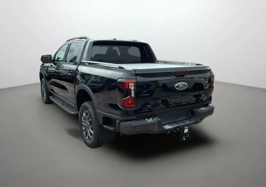 Ford Ranger 2025 noir agate vu 3/4 arrière droit avec attelage et barres de toit visibles.