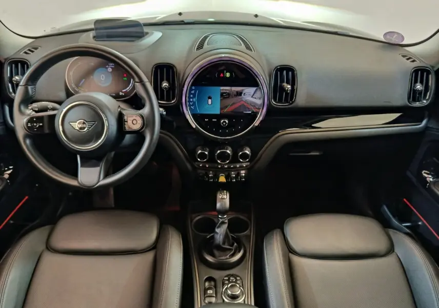 Vue intérieure frontale du tableau de bord noir du MINI Countryman Cooper SE avec écran tactile circulaire et volant cuir.