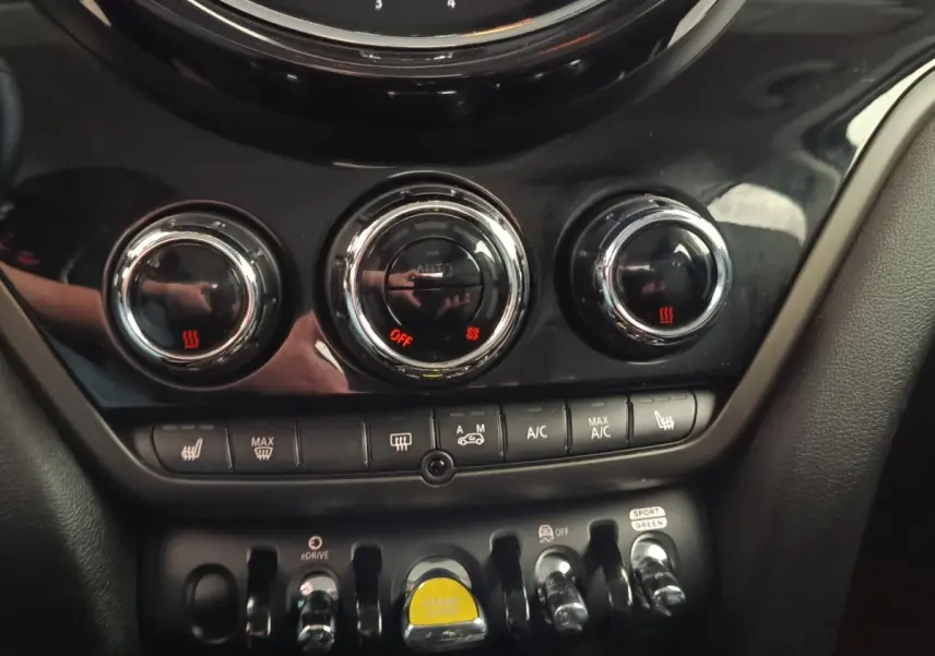 Gros plan sur la console centrale noire du MINI Countryman 2023 avec commandes climatisation et bouton start/stop jaune.