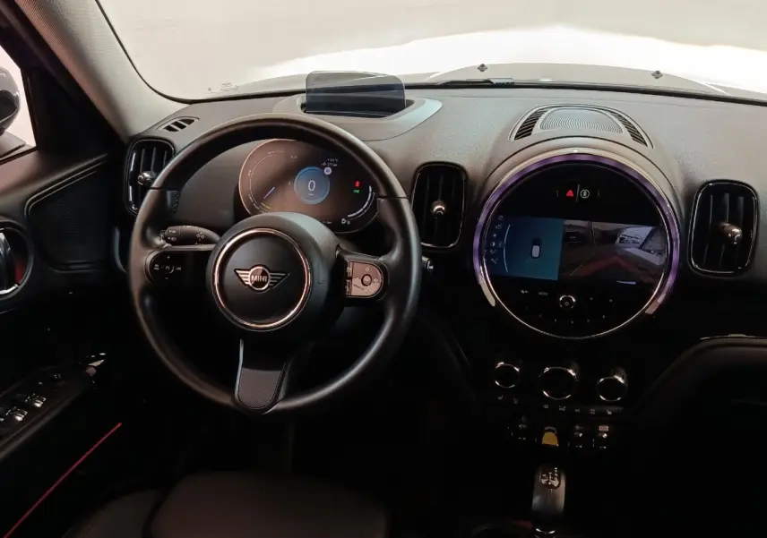 Vue intérieure du tableau de bord noir du MINI COUNTRYMAN Cooper SE avec volant multifonctions et écran tactile central rond.