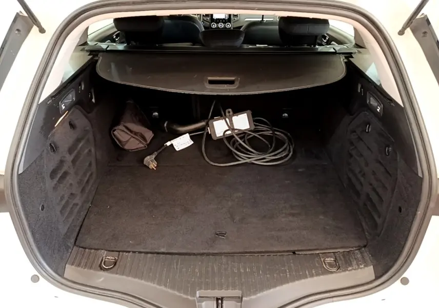 Coffre ouvert d’une Renault Mégane Business E-Tech hybride blanche, avec câble de recharge visible et cache-bagages déployé.