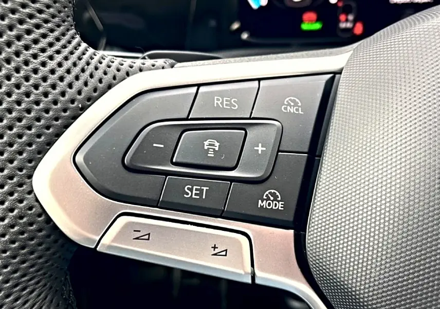 Gros plan sur les commandes multifonctions côté gauche du volant perforé de la Volkswagen Golf noire 2026.