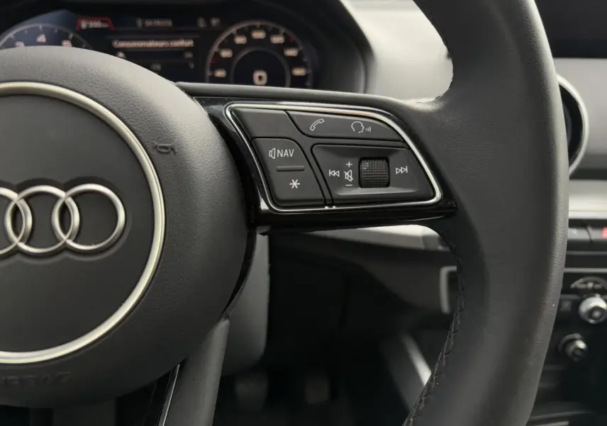 Gros plan sur le volant cuir noir multifonction de l'Audi Q2 30 TFSI 110 S-Line 2024 avec commandes audio visibles