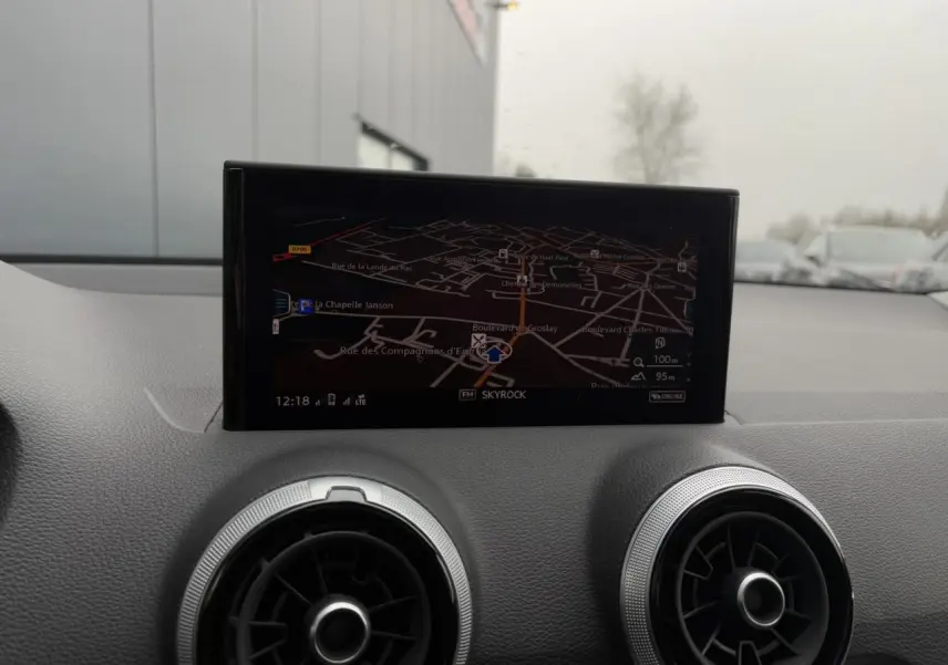 Écran de navigation allumé au centre du tableau de bord d'un Audi Q2 blanc Glacier, avec aérateurs ronds argentés visibles.