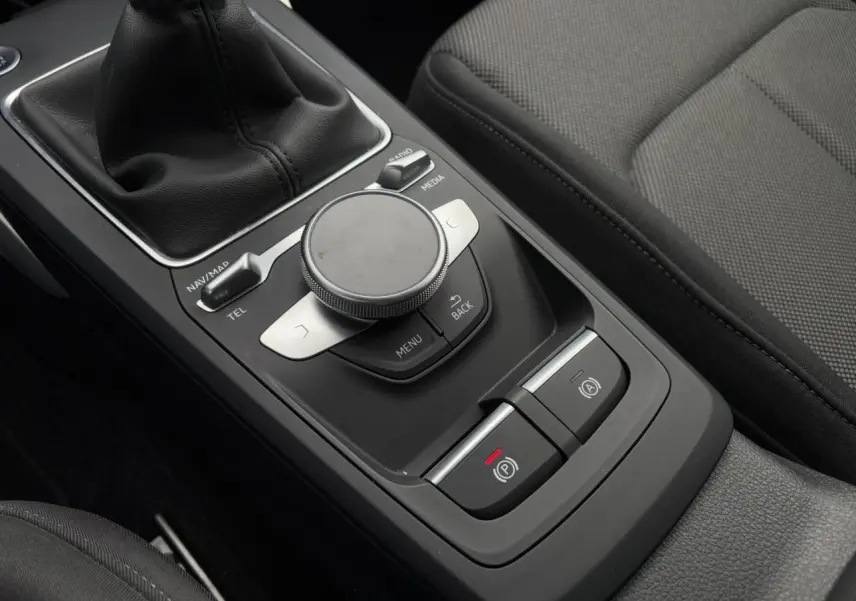 Vue rapprochée de la console centrale noire de l'Audi Q2 30 TFSI 110 S-Line avec commande MMI et frein à main électronique.