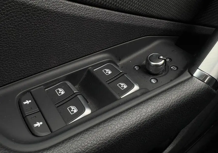 Gros plan sur les commandes de lève-vitres et réglage des rétroviseurs côté conducteur d'Audi Q2 30 TFSI blanc Glacier.