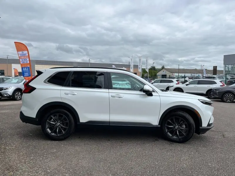 Profil droit du Honda CR-V 2024 blanc platine nacré avec jantes alliage noires et barres de toit visibles.