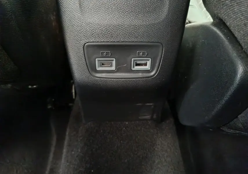 Prise USB type A et USB-C pour recharge, vue rapprochée de la console arrière en plastique noir du Peugeot 208 gris clair.