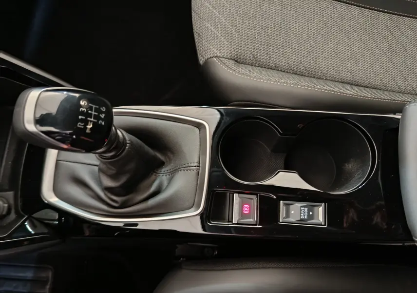Vue rapprochée de la console centrale noire brillante avec levier de vitesses manuel et porte-gobelets du Peugeot 208 gris clair.