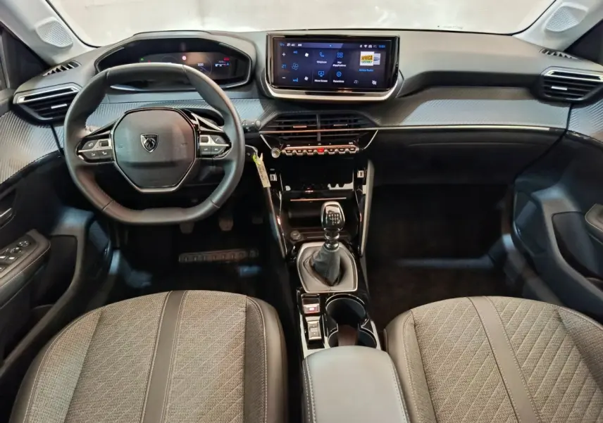 Intérieur Peugeot 208 PureTech 100 S&S Allure 2025, vue frontale du tableau de bord avec volant cuir et écran tactile central.