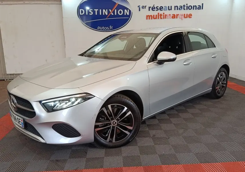 Mercedes Classe A 250 e Business Line gris clair vue 3/4 avant droit en intérieur showroom avec jantes noires et chromées.