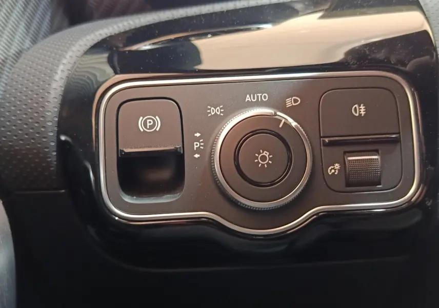 Gros plan sur le panneau de commande des phares et du frein à main électrique dans un Mercedes Classe A gris clair 2023.