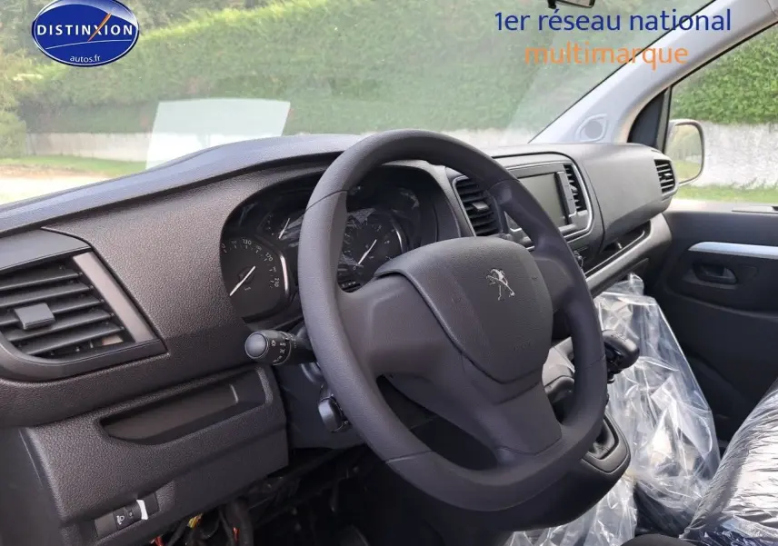 Vue intérieure côté conducteur du Peugeot Expert Blanc Kaolin 2023, volant et tableau de bord en plastique noir.